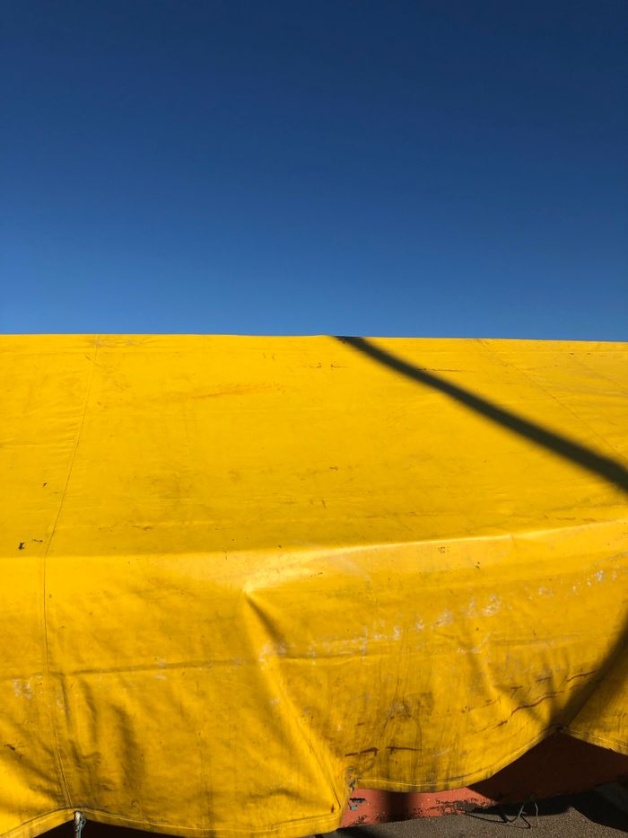 A bright yellow tarpaulin covers a boat, with a clear blue sky as the backdrop, creating a vivid contrast.